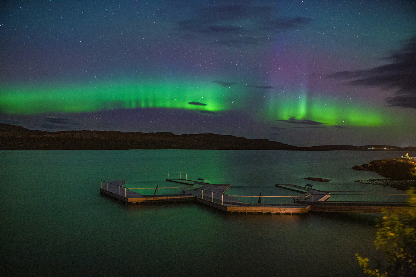 Vök baths at night with northern lights dancing in the sky