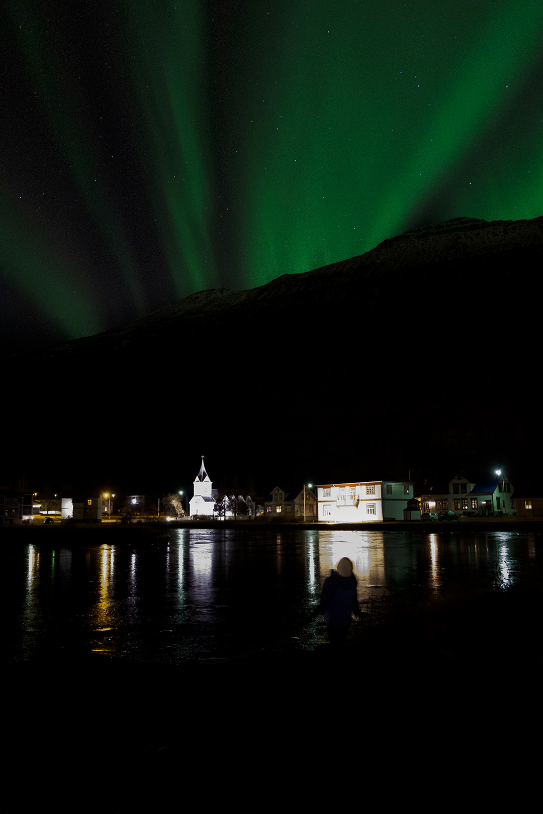 A boy enjoying northern lights show over the Blue church in Seyðisfjörður